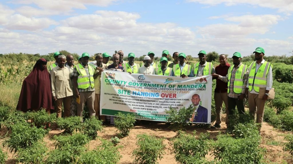 Officials and community members holding the FSRP site handing over banner at an irrigation site in Mandera County