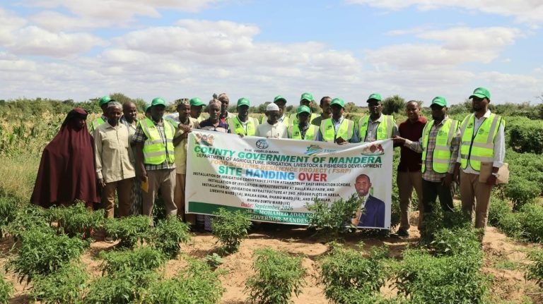 Officials and community members holding the FSRP site handing over banner at an irrigation site in Mandera County